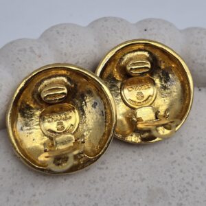 CHANEL - złote okrągłe klipsy vintahe z tłoczonym logo zbliżenie na sygnaturę