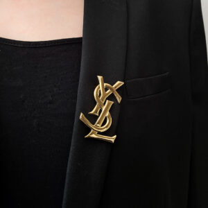 YSL - kultowa złota broszka vintage z monogramem na modelce