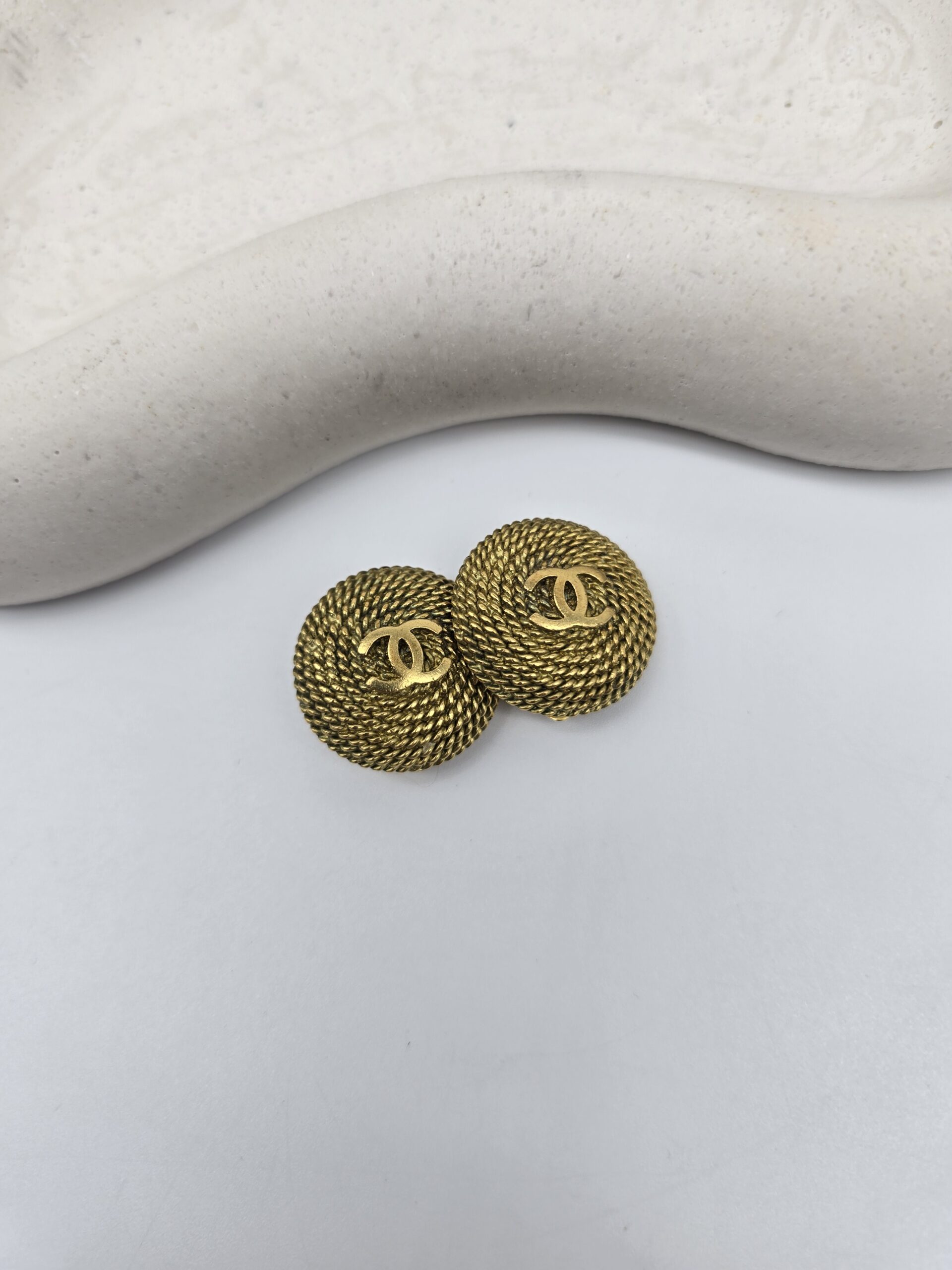 CHANEL - złote klipsy vintage z motywem CC obok siebie